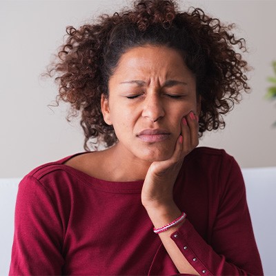Woman experiencing jaw pain holding her jaw on one side