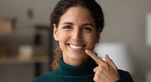 Woman in green turtleneck pointing to her smile