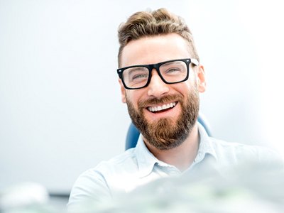 man with glasses smiling in dental chair