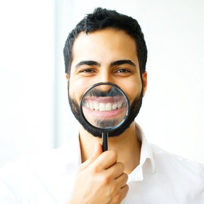 man in white dress shirt holding magnifying glass to his smile