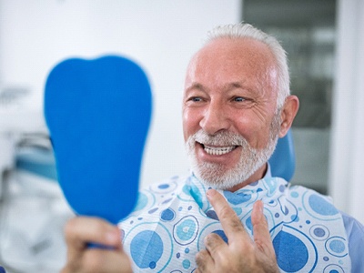 An older man admiring his new and improved smile in the mirror at the dentist’s office