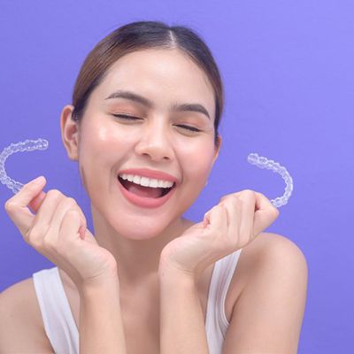 Woman holding two Invisalign trays and smiling excitedly 