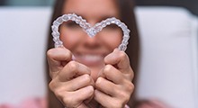 Woman holding up two Invisalign trays to make a heart shape