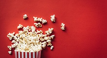 A movie-theater style popcorn bucket spilling out onto a red background