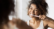 Woman smiling and brushing her teeth in mirror