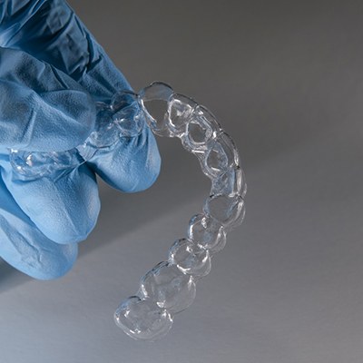 Gloved hand holding clear aligner.