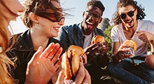 Group of friends smiling while eating lunch outside