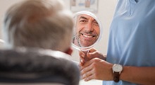 Man examining smile in mirror with emergency dentist in McKinney