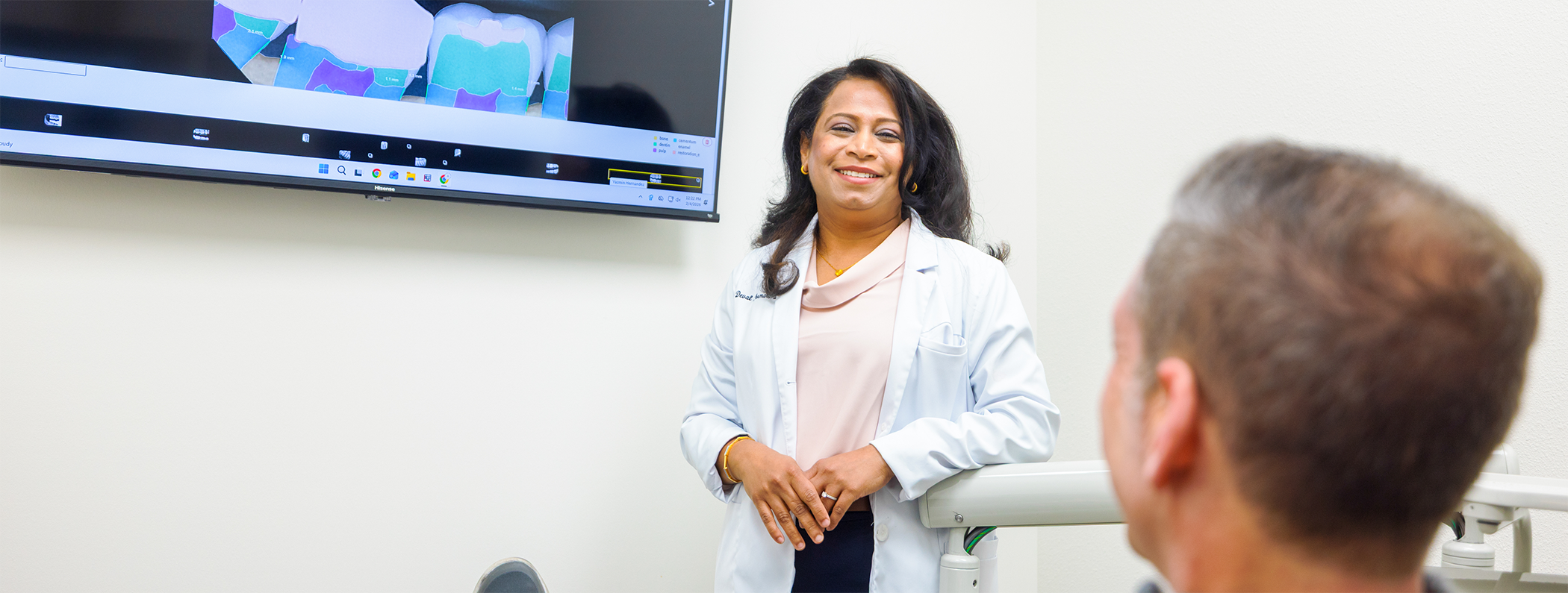 Dentist standing next to monitor and smiling at patient