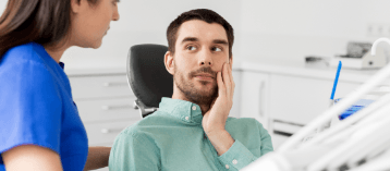 Man in dental chair holding cheek