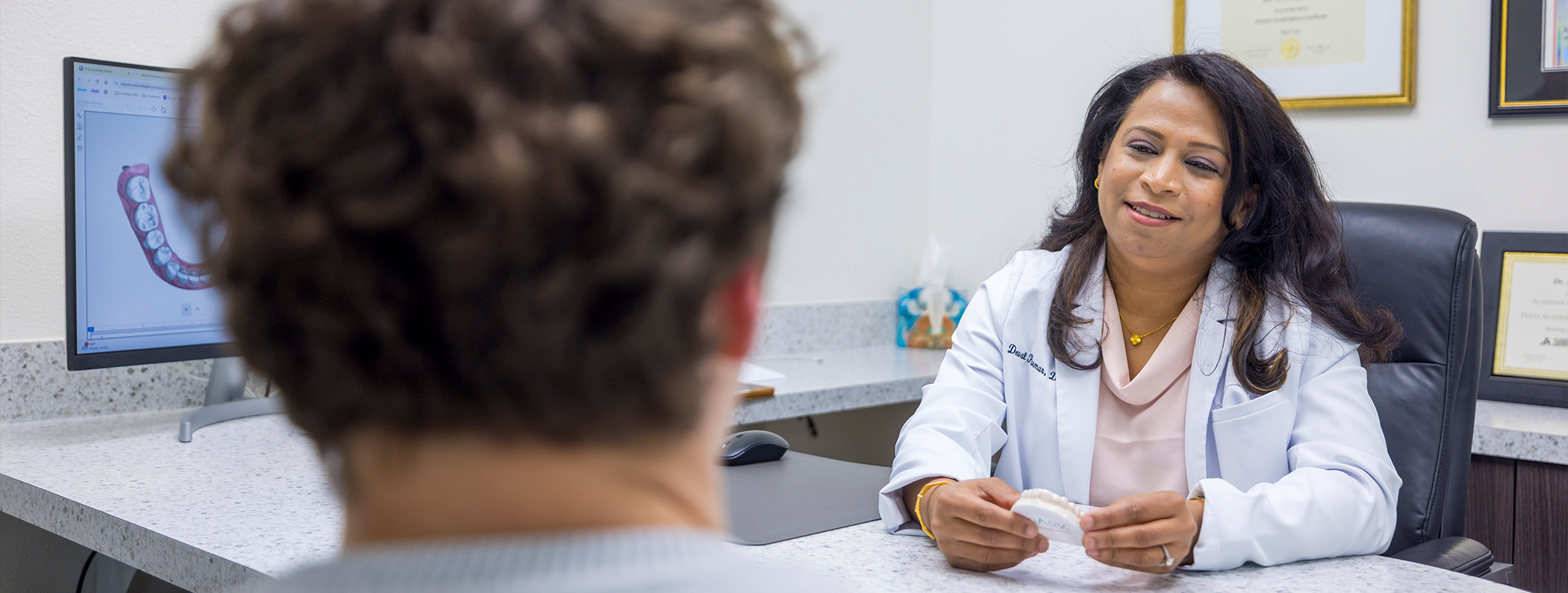 McKinney dentist sitting at desk speaking to patient while holding mold of teeth